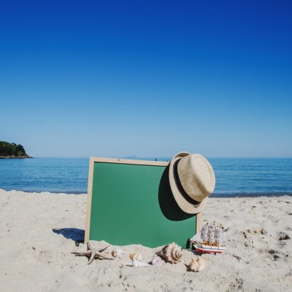 Ein Hut hängt an einer Tafel, die in den Sandstrand gesteckt ist